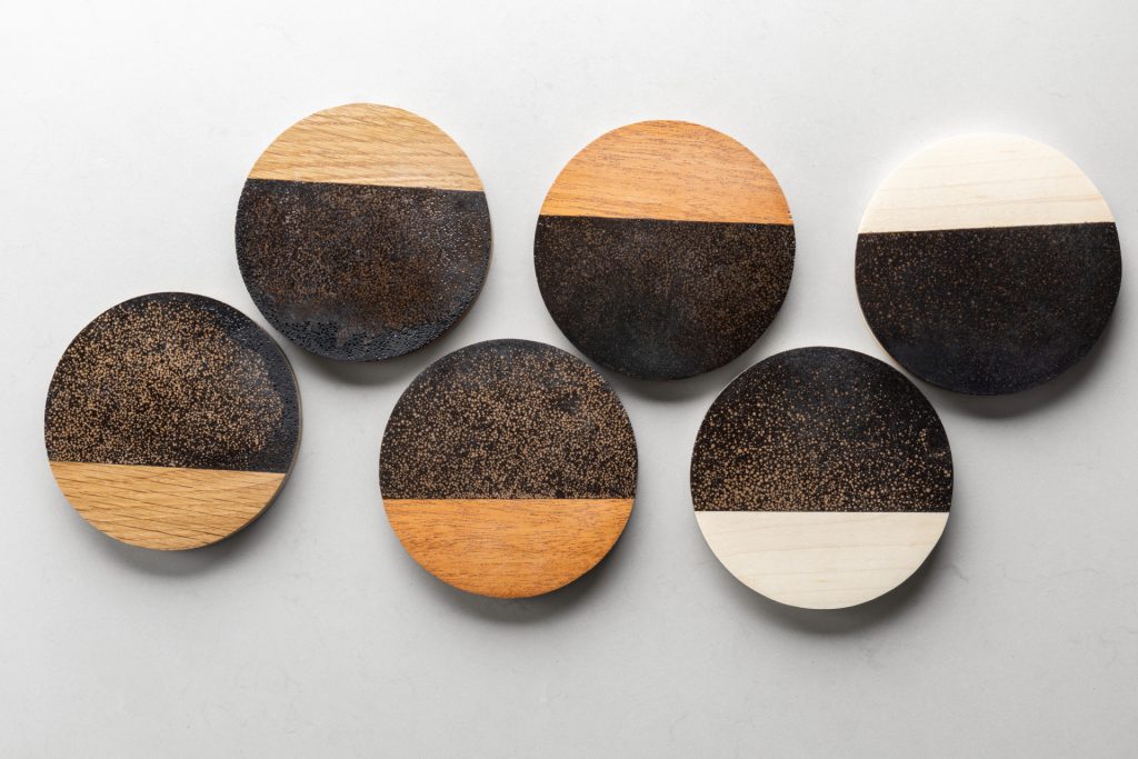 Set of six round coasters showing natural wood and dark coffee ground texture arranged on white surface