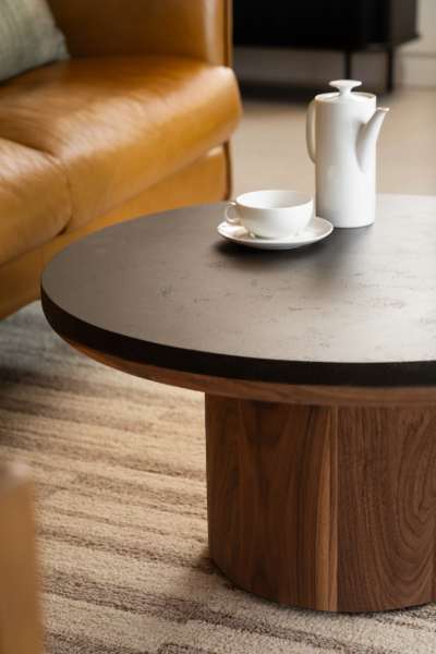 Round coffee table with dark coffee ground surface and natural wood base, styled with glass teapot and cups on leather tan sofa background