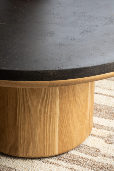 Round coffee table with dark coffee ground surface and natural wood base, styled with glass teapot and cups on beige sofa background