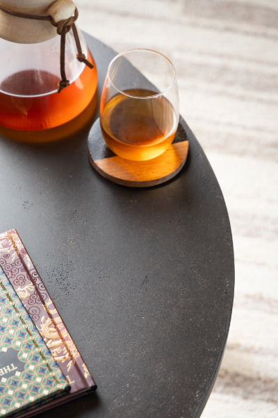 Round coffee table with dark coffee ground surface and natural wood base, styled with glass teapot and cups on beige sofa background