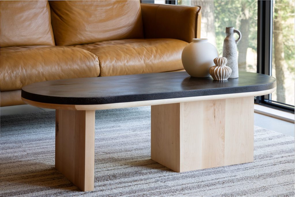 Oval pill-shaped coffee table with coffee shell finish and maple wood base styled with ceramic accessories