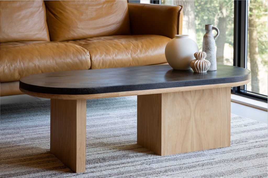 Oval pill-shaped coffee table with coffee shell finish and oak wood base styled with ceramic accessories