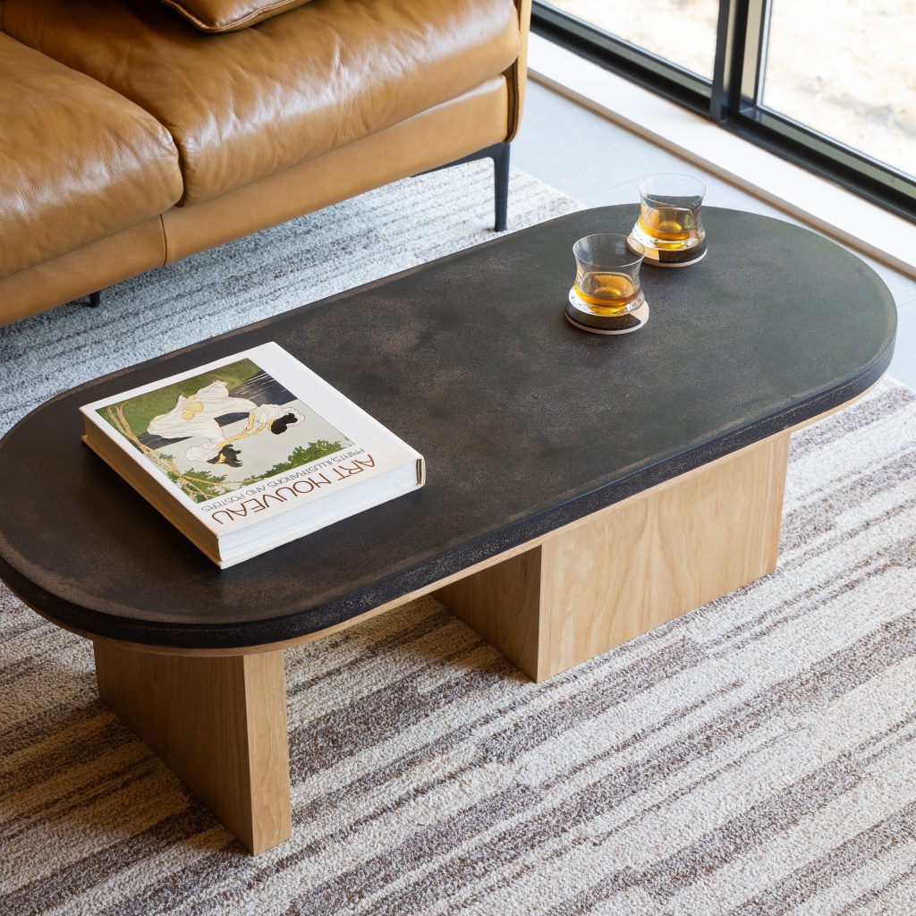 Oval pill-shaped coffee table with coffee shell finish and maple wood base styled with ceramic accessories
