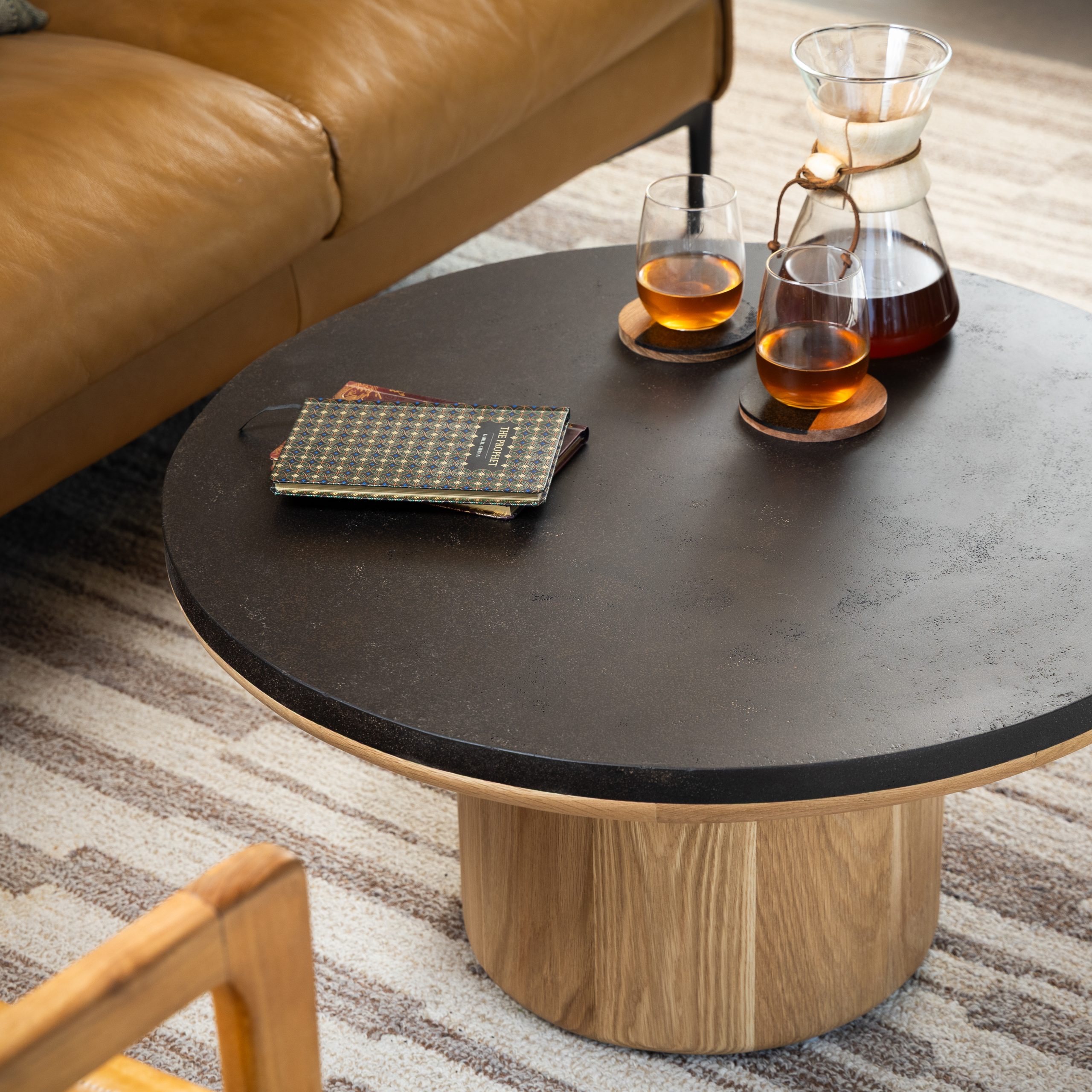 Round coffee table with dark coffee ground surface and natural wood base, styled with glass teapot and cups on beige sofa background